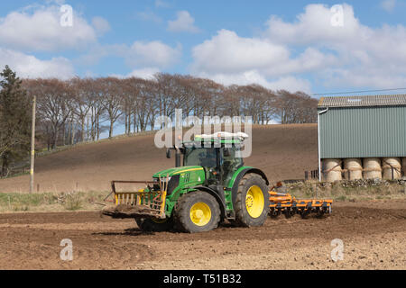 Eine grüne John Deere Traktor und ein Simba Unipress Kultivator bei der Arbeit in die schottische Landschaft, mit einer Linie der Buche am Horizont Stockfoto