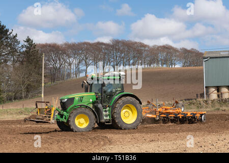 Eine grüne John Deere Traktor und ein Simba Unipress Kultivator bei der Arbeit in die schottische Landschaft, mit einer Linie der Buche am Horizont Stockfoto