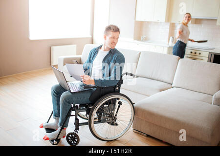 Attraktive junge Kursteilnehmer mit Integration und Behinderung. Das Sitzen auf einem Stuhl und zurück zu schauen. Junge Frau Kochen am Herd. Blick einander an. Coup Stockfoto