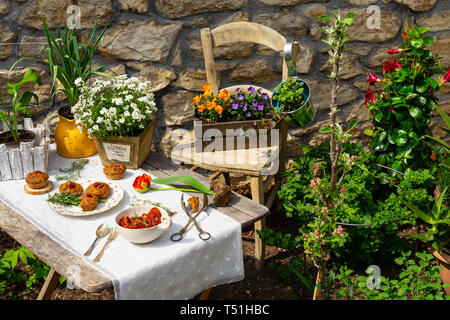 Romantisches Abendessen auf einem Gartentisch mit blühenden Blumen und Pflanzen Stockfoto