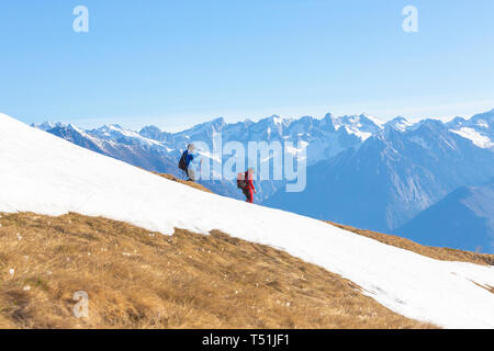 Wanderer auf verschneiten Kamm in Alpe Combanina mit Valmasino im Hintergrund, Bergamasker Alpen, Val Gerola, Valtellina, Lombardei, Italien Stockfoto