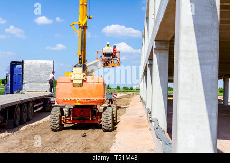 Rigger ist in der hohen erhöhten Cherry Picker, er bewegt sich über die Baustelle. Stockfoto