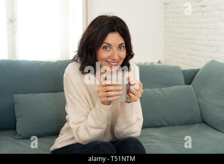 Lifestyle Portrait von jungen recht entspannt Frau trinkt Kaffee oder Schokolade Gefühl glücklich und gemütlich zu Hause glücklich lächelnd auf der Couch. In leisur Stockfoto