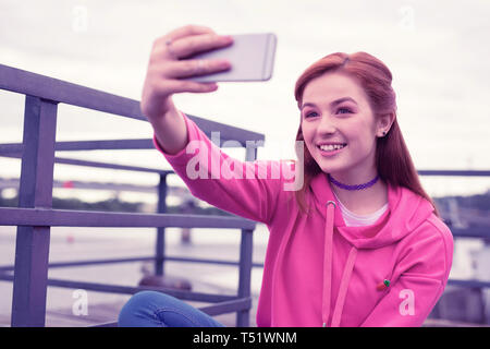 Langhaarige hübsches Mädchen tragen leuchtend rosa Hoodie und selfie Stockfoto