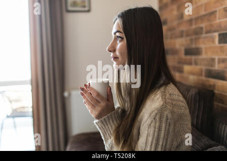 Schöne Frau entspannt auf dem Sofa zu Hause, Fernsehen und genießen Kaffee Stockfoto