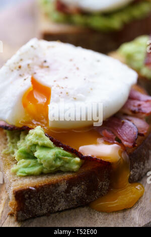 Pochiertes Ei Toasts mit Avocado und Speck. Auf einem Holzbrett serviert, hohe Auflösung Stockfoto