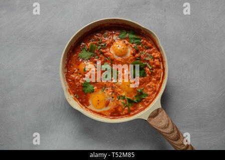 Shakshuka, Naher Osten das traditionelle, hausgemachte Frühstück - Spiegeleier, Zwiebel, Paprika, Tomaten und Petersilie in einer Pfanne auf einem dunklen Hintergrund Stockfoto