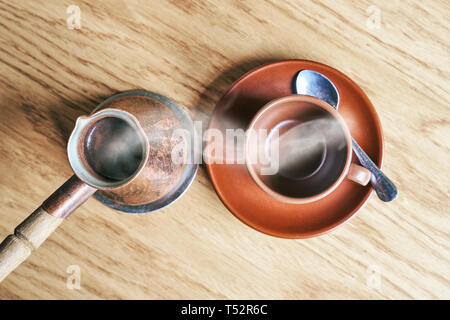 Kaffee in orientalischen Türkischen Stil in cezve serviert, einem kleinen langstieligen Pot mit einem Ausguss und Schale auf einem Holztisch Stockfoto