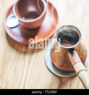 Kaffee in orientalischen Türkischen Stil in cezve serviert, einem kleinen langstieligen Pot mit einem Ausguss und Schale auf einem Holztisch Stockfoto