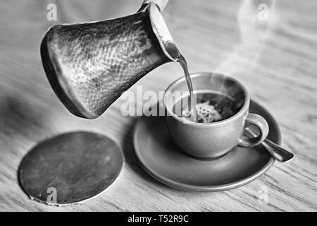 Kaffee in orientalischen Türkischen Stil in cezve serviert, einem kleinen langstieligen Pot mit einem Ausguss und Schale auf einem Holztisch Stockfoto