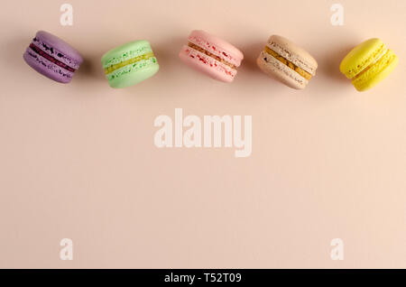 Bunte Makronen oder MACARONS in einer Reihe auf Pastell beige Hintergrund. Gruß oder einladungskarte Konzept. Keine Diät Tag Stockfoto