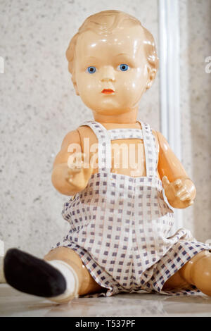 Ein altes Spielzeug ist ein Vintage Doll mit blauen Augen, in einem Overall gekleidet. Aus der Vergangenheit betrifft. Bild vertikal. Stockfoto