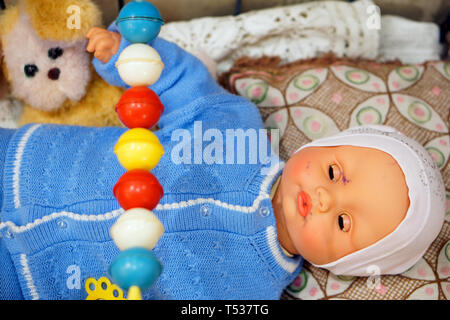 Altes Spielzeug, Vintage Doll - Baby in einem blauen Pullover in eine Krippe mit einem Hund. Aus der Vergangenheit betrifft. Stockfoto