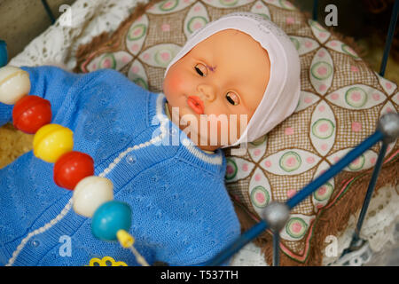 Altes Spielzeug, Vintage Doll - Baby in einem blauen Pullover in einer Krippe. Aus der Vergangenheit betrifft. Stockfoto