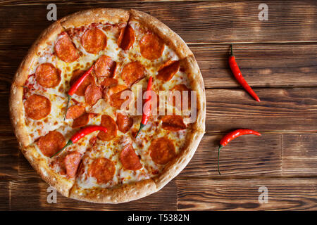 In Scheiben geschnittene hausgemachte Pizza mit Salami und red chili peppers liegt auf einem natürlichen Holz- Oberfläche von Pine Planken. Tageslicht. Stockfoto