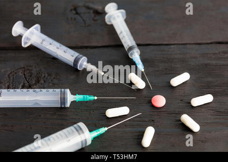 Medizinische Spritzen von verschiedenen Kapazitäten, Kapseln, Tabletten liegen auf einer alten schwarzen Brett, und zeigen Sie auf einem roten runden Tablette. Stockfoto