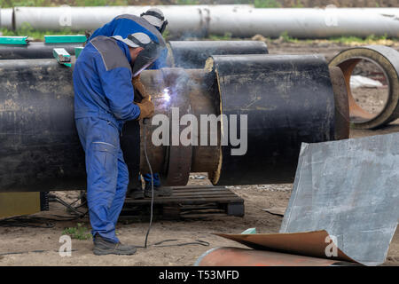 Schweißer Schweißen Gelenke auf große isolierte Stahl Fernwärme Rohr mit elektrischem Schweißen. Tragen Fangvorrichtungen. Stockfoto