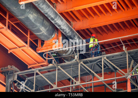 Arbeitnehmer Schweißarbeiten auf Fernwärme Rohrleitungen unter Metal Bridge. Große Pipeline Installation funktioniert. Stockfoto