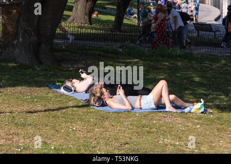Zwei junge Frauen in der Sonne zu liegen in einem Park können Sie über Ihr Mobiltelefon Stockfoto
