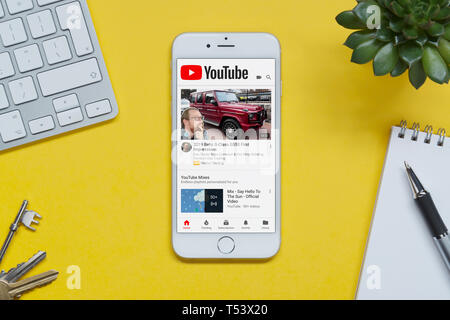 Ein iPhone mit der YouTube-Website ruht auf einem gelben Hintergrund Tabelle mit einer Tastatur, Tasten, Notepad und Anlage (nur redaktionelle Nutzung). Stockfoto