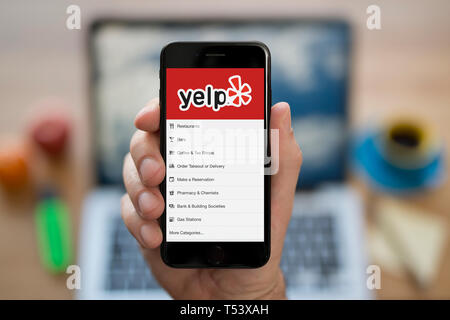 Ein Mann schaut auf seinem iPhone die zeigt die Yelp Logo (nur redaktionelle Nutzung). Stockfoto