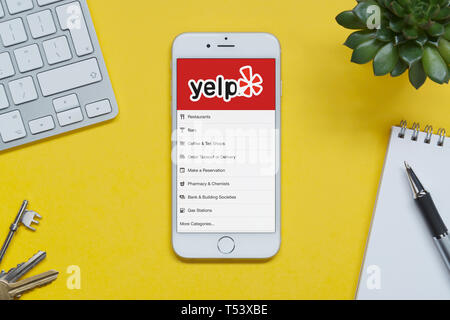 Ein iPhone mit Yelp website ruht auf einem gelben Hintergrund Tabelle mit einer Tastatur, Tasten, Notepad und Anlage (nur redaktionelle Nutzung). Stockfoto