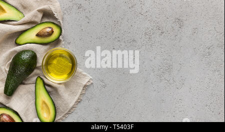 In Scheiben geschnitten und ganze Avocados und Öl in der Schale auf der Serviette über konkreten Hintergrund top anzeigen, kopieren. Stockfoto