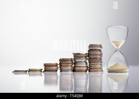 Nahaufnahme der Sanduhr in der Nähe von Stapel von Münzen über Schreibtisch Stockfoto