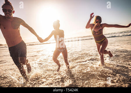 Freunde kaukasischen Gruppe von Menschen Mann und zwei Frauen genießen und gemeinsam Spaß haben in der Freundschaft in den Sommerferien läuft aus dem Wasser - Sonnenuntergang Stockfoto