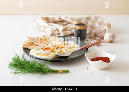 Schale mit Türkischen Cilbir Eier, Joghurt, pochierte Eier, Knoblauch, Chili, frischer Dill und zerlassener Butter. Verziert mit wenigen Stücke von lavash Brot ein Stockfoto