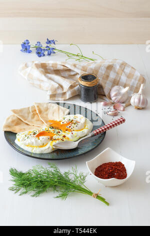 Schale mit Türkischen Cilbir Eier, Joghurt, pochierte Eier, Knoblauch, Chili, frischer Dill und zerlassener Butter. Verziert mit wenigen Stücke von lavash Brot ein Stockfoto