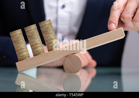 Geschäftsmann Balancing gestapelte Münzen mit Finger auf Holz- Wippe über reflektierende Schreibtisch Stockfoto