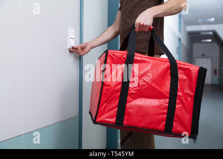 Pizza Delivery Man Läuten der Türklingel mit einer großen Tüte in der Hand Stockfoto