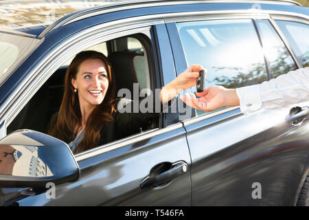 Lächelnde junge Frau sitzt im Auto und Auto Schlüssel zur männlichen Hand Stockfoto