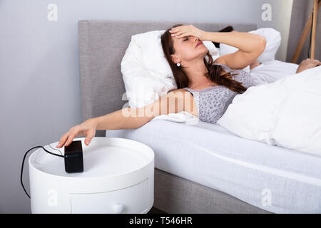 Junge Frau schlafend auf dem Bett Ausschalten Wecker im Schlafzimmer Stockfoto