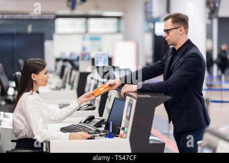 Business Reise. Hübscher junger Geschäftsmann in Anzug Holding seinen Pass und im Gespräch mit Frau am Check-in-Schalter im Flughafen Stockfoto