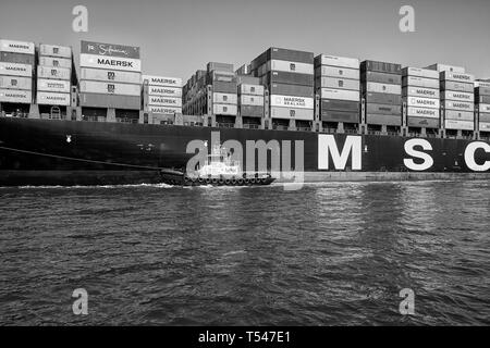 Schwarz-weiß-Foto von AmNav Tractor Tug (Tugboat), INDEPENDENCE, Guiding the Container Ship, MSC ELODIE im Hafen von Long Beach, USA. Stockfoto