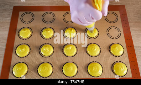 Konditor gießt Teig aus gebäckbeutel auf Schablone Silikon Matte auf dem Tisch, Blick von oben. Kochen Makronen, close-up. Stockfoto