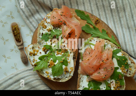 Zwei Sandwiches mit Lachs, Olivenöl, Rucola und Frischkäse, serviert auf dem Holzbrett. Gesunde trendy leckeres Frühstück. Ein Löffel aus Holz mit m Stockfoto