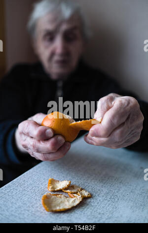 Eine alte Frau reinigt Tangerine, Hände, Nahaufnahme. Stockfoto