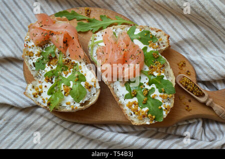 Lachs belegte Brote mit Frischkäse, Senf und Rucola auf dem Holzbrett. Gesunde Ernährung im Trend. Perfektes Frühstück. Stockfoto