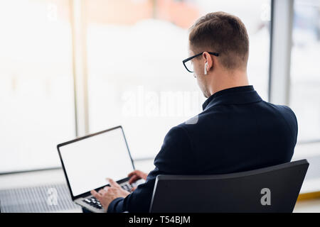 Young Business Mann sitzt auf dem Computer mit moderner, stilvoller drahtlose Kopfhörer warten am Flughafen für den Flug Stockfoto