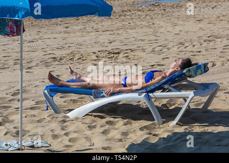 Bournemouth, Dorset, Großbritannien. 21. Apr 2019. UK Wetter: Die hitzewelle weiter mit warmem und sonnigem Wetter, wie Beachgoers Kopf zum Meer die Wärme und Sonnenschein in Bournemouth Strände für Ostern - Mitte Morgen und schon Strände zu genießen sind verpackt, als Sonnenanbeter gehen Sie früh in ihrem Lebensraum zu erhalten. Frau in Blau Bikini Sonnenbaden auf der Sonnenliege. Credit: Carolyn Jenkins/Alamy leben Nachrichten Stockfoto