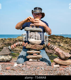 Dunbar, East Lothian, Schottland, Großbritannien. 21. Apr 2019. Europäische Stein stacking Meisterschaft: Harry Maddox, aus England, Salden Steine in den künstlerischen Wettbewerb, so dass Wettbewerber 3 Stunden nichts von Steinen oder gefundene Gegenstände in Augenhöhe Cave Beach zu erstellen Stockfoto