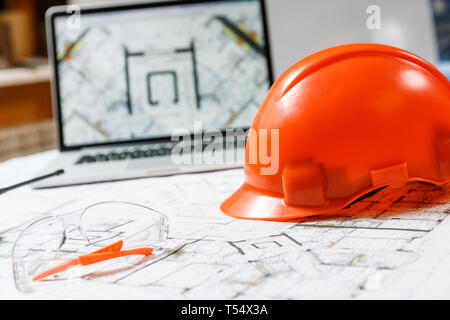 Orange Schutzhelm, Laptop mit Zeichnungen und Schutzbrille mit Blueprints auf einen Tisch. Architektur und Bau Konzept Stockfoto