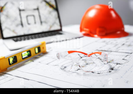 Bau Schutzbrille, orange Schutzhelm, Laptop mit Zeichnungen, Level Meter liegen in einem Blueprints auf einen Tisch. Architektur und Bau Stockfoto