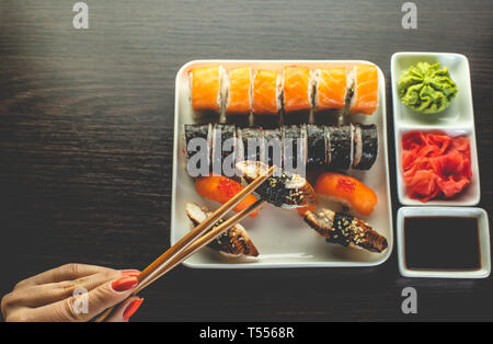 Weibliche hand nimmt Sushi mit Aal Stäbchen Stockfoto