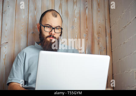Bärtiger Mann mit Brille, der an einem Notebook arbeitet. Stockfoto