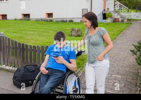 Mutter mit behinderten Sohn warten auf den Schulbus Stockfoto