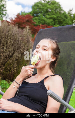 Jugendmädchen Eis am Stiel essen in einem Liegestuhl im Garten Stockfoto